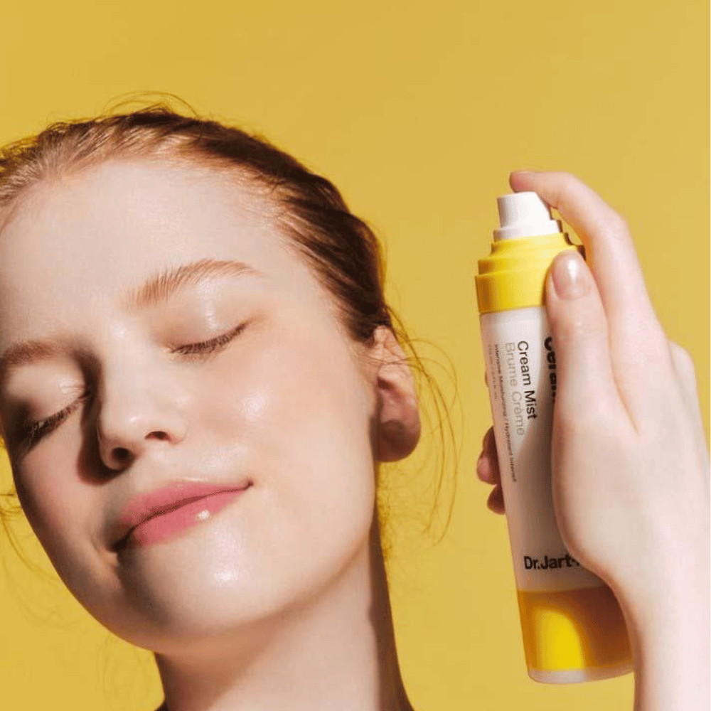 En kvinne holder en flaske Dr. Jart+ Ceramidin Cream Mist 110ml i ansiktet, som fremmer dens fuktighetsboost-fordeler og veganske formulering.