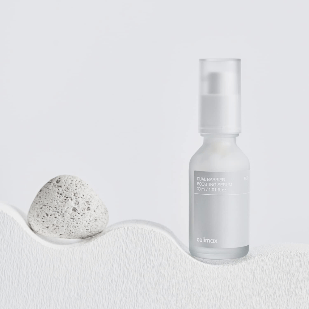 Celimax Dual Barrier Boosting Serum plassert på tekstil med stein, rolig produktbilde som signaliserer fuktighet og styrket hudbarriere.