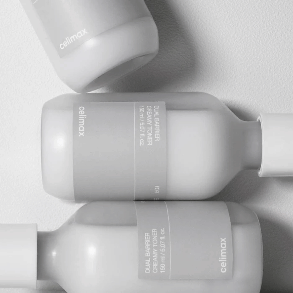 Tre liggende flasker av Celimax Dual Barrier Creamy Toner i et minimalistisk design med grå etikett og mykt lys – perfekt for sensitiv og tørr hud.