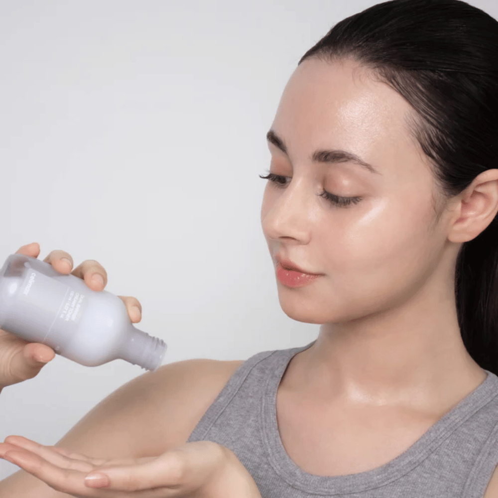 Kvinne med glansfull, fuktet hud påfører Celimax Dual Barrier Creamy Toner ved å helle produktet i håndflaten før sin hudpleierutine.