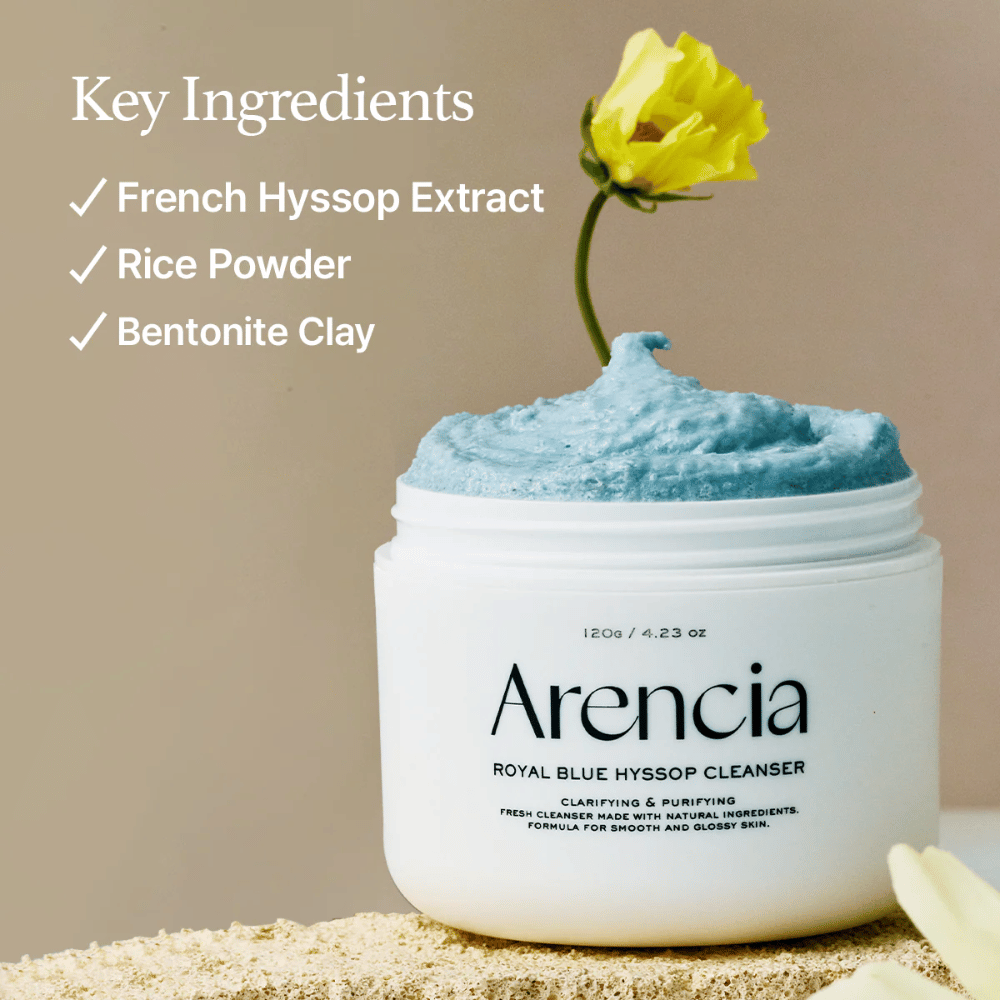 Bilde av krukken "Arencia Royal Blue Hyssop Cleanser" fylt med blå rengjøringskrem. En gul blomst stikker opp fra kremen. Teksten i bildet fremhever tre nøkkelingredienser: French Hyssop Extract, Rice Powder og Bentonite Clay.
