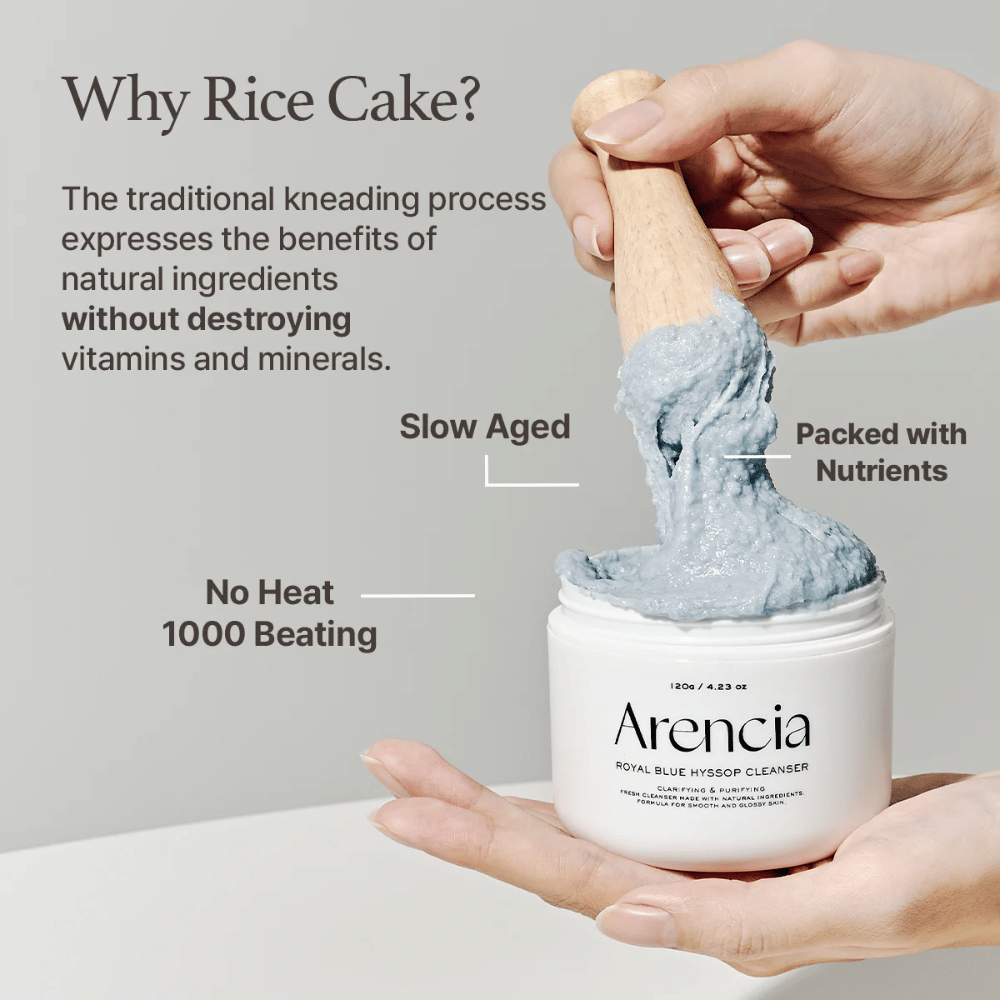 Hånd som holder rengjøringskrukken "Arencia Royal Blue Hyssop Cleanser" med en tresleiv som løfter opp den blå, mochi-lignende rengjøringspastaen. Tekst i bildet beskriver fordeler med risdeigsprosessen, som "No Heat", "1000 Beating", "Slow Aged" og "Packed with Nutrients".