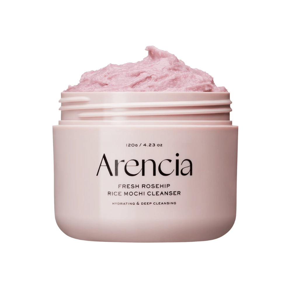 Nærbilde av en rosa krukke med Arencia Royal Rosehip Cleanser, fylt med rosa rengjøringskrem med pisket, mochi-lignende tekstur. Teksten på krukken viser at produktet fukter og renser i dybden.