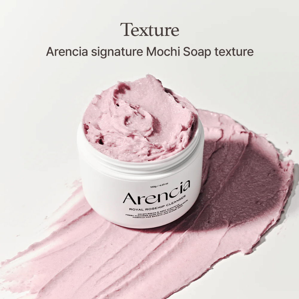 Krukke med Arencia Royal Rosehip Cleanser sees på toppen av en utsmurt rosa rengjøring med mochi-lignende tekstur. Teksten ovenfor beskriver produktet som Arencias signaturtekstur.