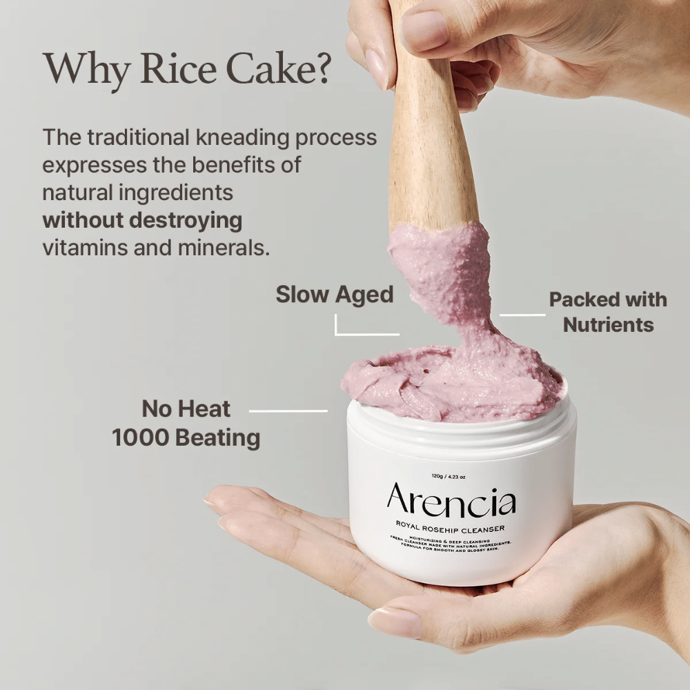 En hånd holder i en åpen krukke av Arencia Royal Rosehip Cleanser, med en rosa, mochi-lignende rengjøringsformel som løftes med en trespatel – viser produktets tekstur og tradisjonelle fremstillingsmetode.