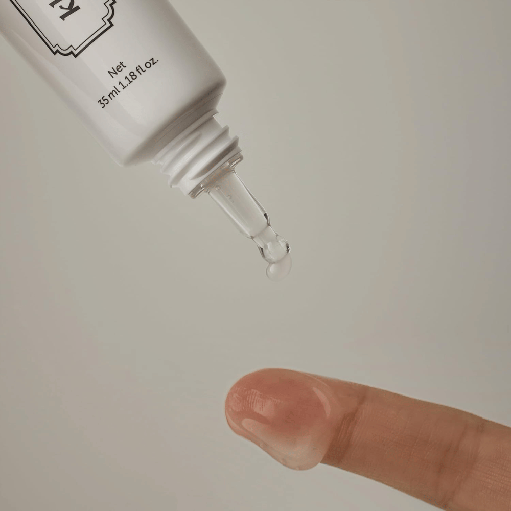 Detaljbilde der en klar, lett gel påføres fra den smale spissen mot en finger. Bildet illustrerer produktets transparente, gelbaserte konsistens og den presise påføringen rundt øyeområdet.