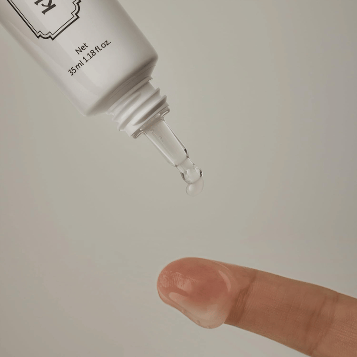 Detaljbilde der en klar, lett gel påføres fra den smale spissen mot en finger. Bildet illustrerer produktets transparente, gelbaserte konsistens og den presise påføringen rundt øyeområdet.