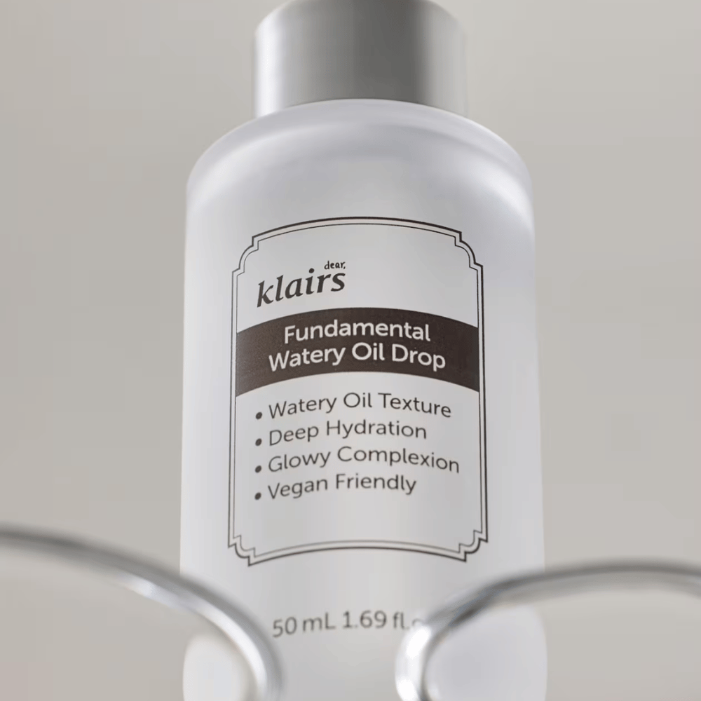 Flaske med Klairs Fundamental Watery Oil Drop, 50 ml, plassert i en gjennomsiktig holder, med tydelig etikett som fremhever produktets fuktighetsgivende og veganske egenskaper.