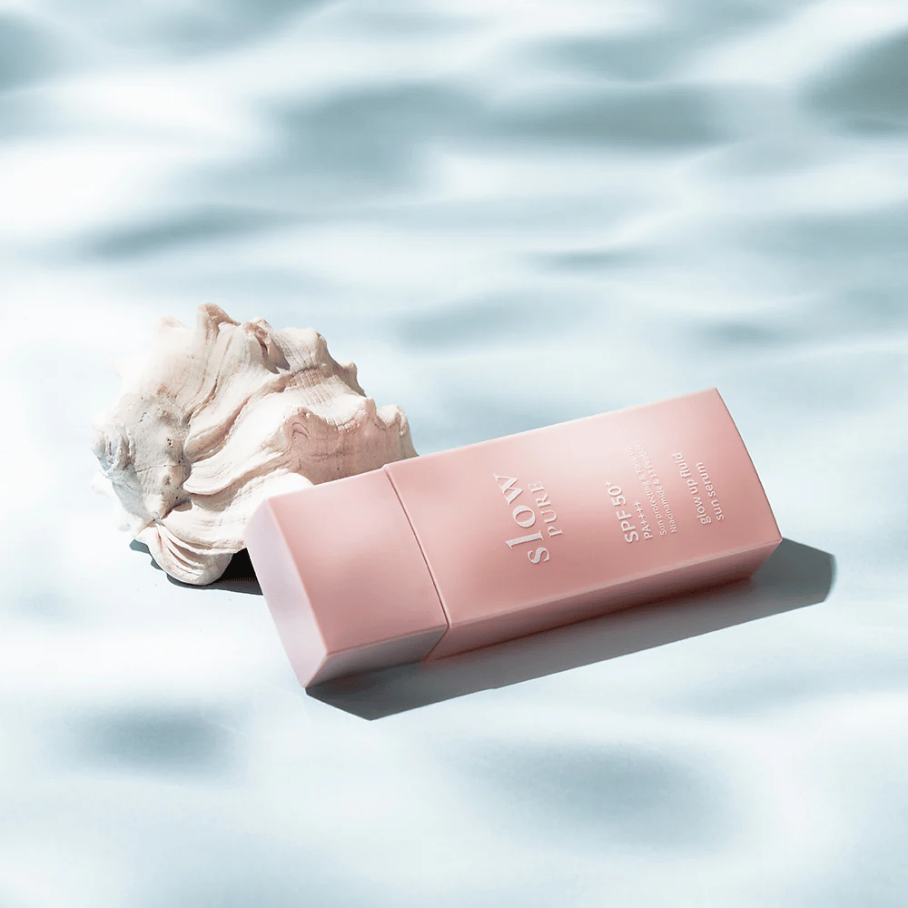 Slow Pure Glow Up Fluid Sun Serum ved skjell og vanneffekt, fremhever solbeskyttelse og glød.