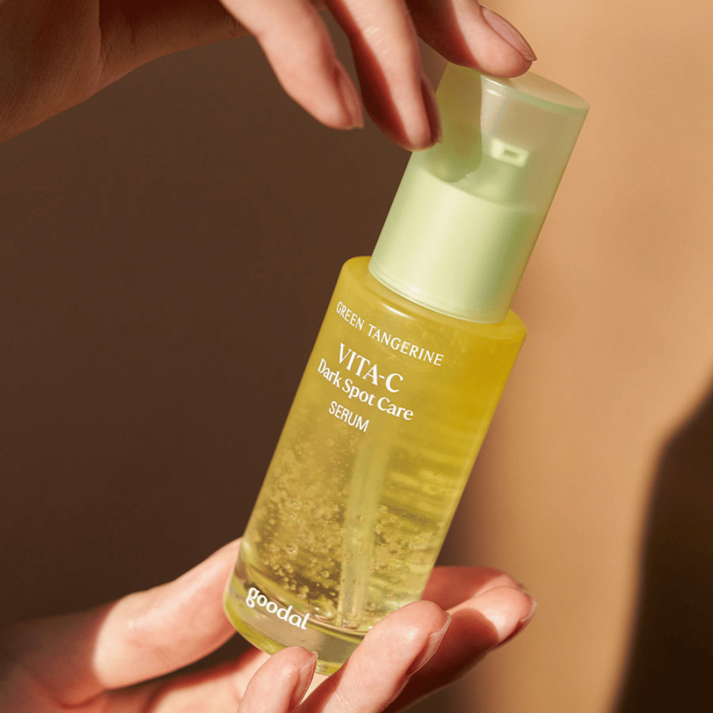 En person som holder en flaske Green Tangerine Vita C Dark Spot Care Serum 40ml fra Goodal for hyperpigmentering og pleie av mørke flekker.