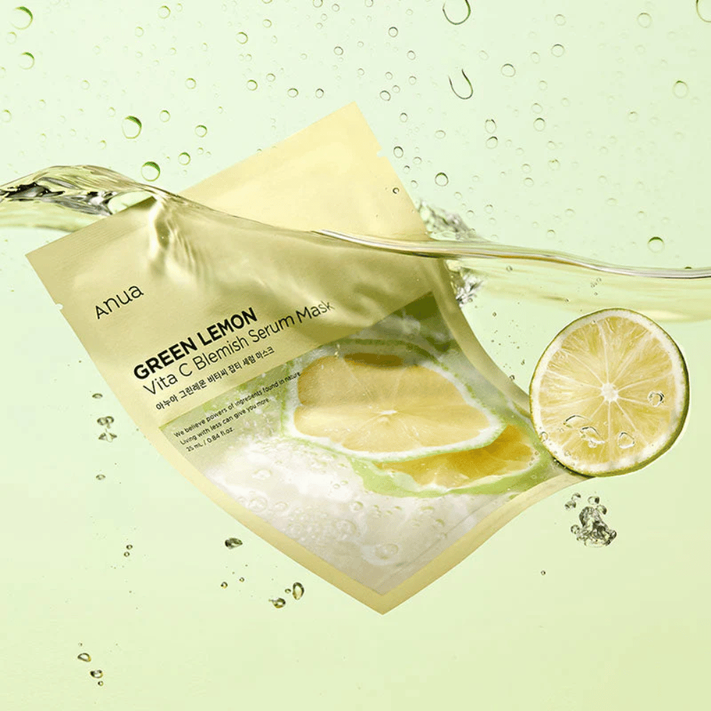 Et livlig bilde av Anua Green Lemon Vita C Blemish Serum Mask emballasje med gjennomsiktige vanndråper og skiver av grønn sitron rundt omkring. Emballasjen er delvis dekket av en strøm av vann på en lys grønn bakgrunn.