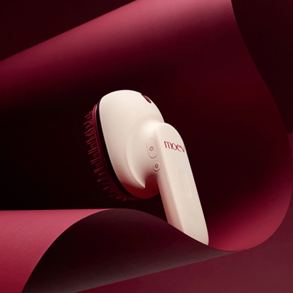 MOEV Hair Steamer Pro i elegant design mot rød bakgrunn. Innovativ hårpleiebørste som bruker damp og varme for å gi glans, mykhet og styrket hårhelse.