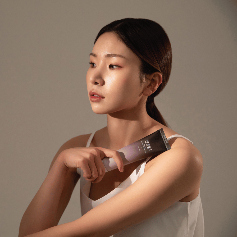 En ung asiatisk kvinne som holder en børste i hånden mens hun bruker Haruharu Wonders Black Rice Moisture 5.5 Soft Cleansing Gel 100ml.