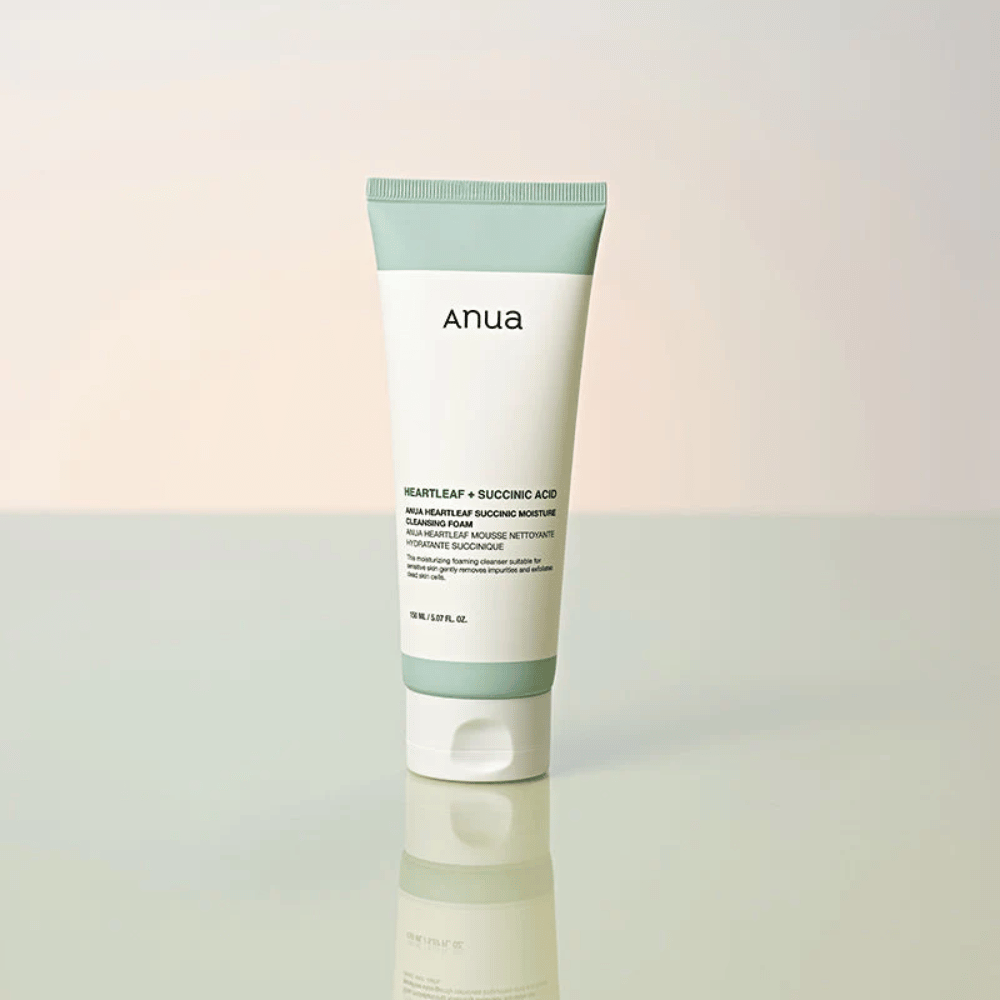 Frittstående produktbilde av Anua Heartleaf + Succinic Acid Moisture Cleansing Foam. Produktet vises stående på en reflekterende overflate som tydelig fremhever emballasjens design og merkevarens stilrene estetikk.