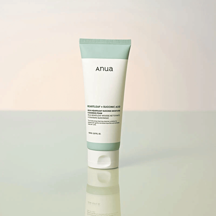 Frittstående produktbilde av Anua Heartleaf + Succinic Acid Moisture Cleansing Foam. Produktet vises stående på en reflekterende overflate som tydelig fremhever emballasjens design og merkevarens stilrene estetikk.