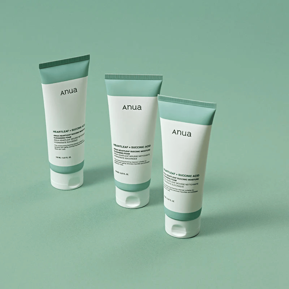 Tre pakninger av Anua Heartleaf + Succinic Acid Moisture Cleansing Foam presentert mot en lysegrønn bakgrunn. Bildet fremhever produktets rene og minimalistiske design samt gir et profesjonelt inntrykk av produktserien.