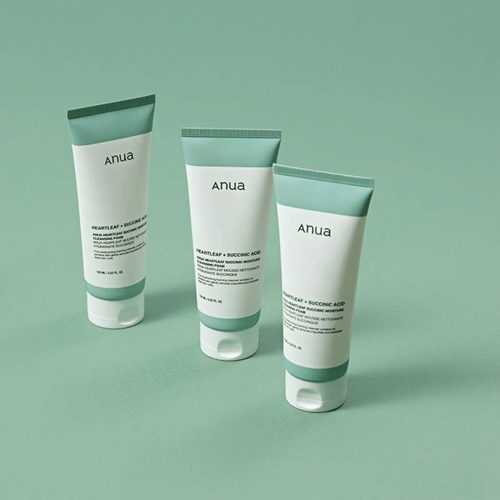 Tre pakninger av Anua Heartleaf + Succinic Acid Moisture Cleansing Foam presentert mot en lysegrønn bakgrunn. Bildet fremhever produktets rene og minimalistiske design samt gir et profesjonelt inntrykk av produktserien.