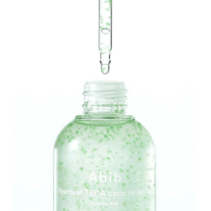 Minimalistisk nærbilde av serumflaske og pipette der den transparente formelen med grønne kapsler står i fokus mot lys bakgrunn.
