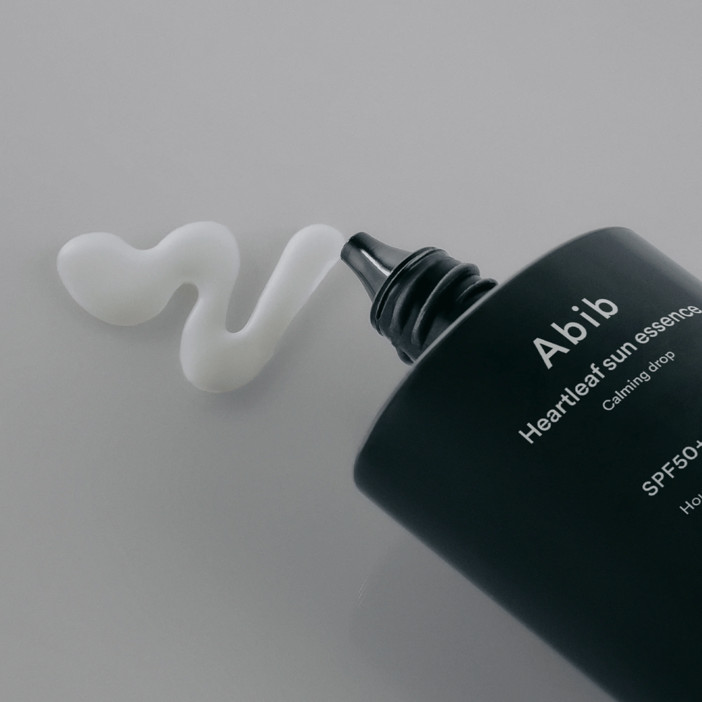 Nærbilde av Abib Heartleaf Sun Essence Calming Drop med solkremen presset ut i en hvit, bølget linje på en lys overflate.
