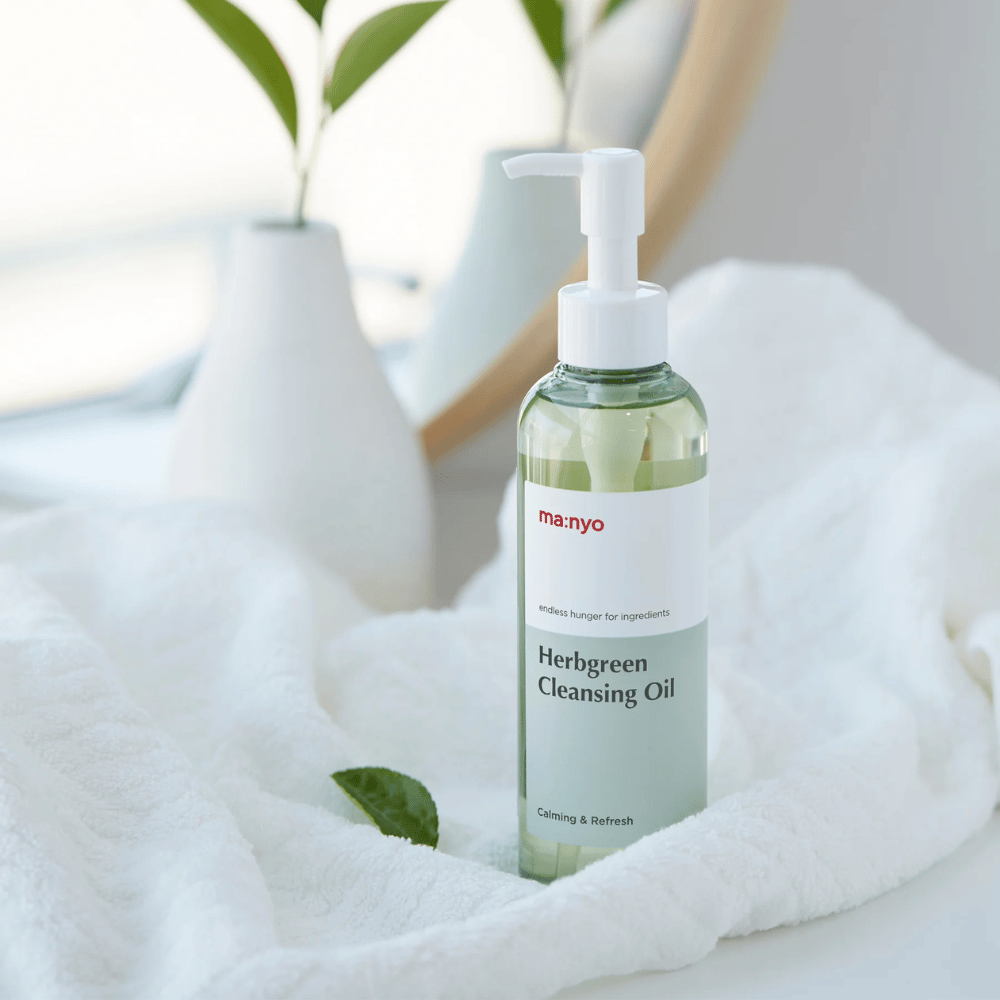ma:nyo Herbgreen Cleansing Oil i pumpeflaske plassert på hvit håndkle, beroligende renseolje med urtebaserte ingredienser for skånsom ansiktsrengjøring