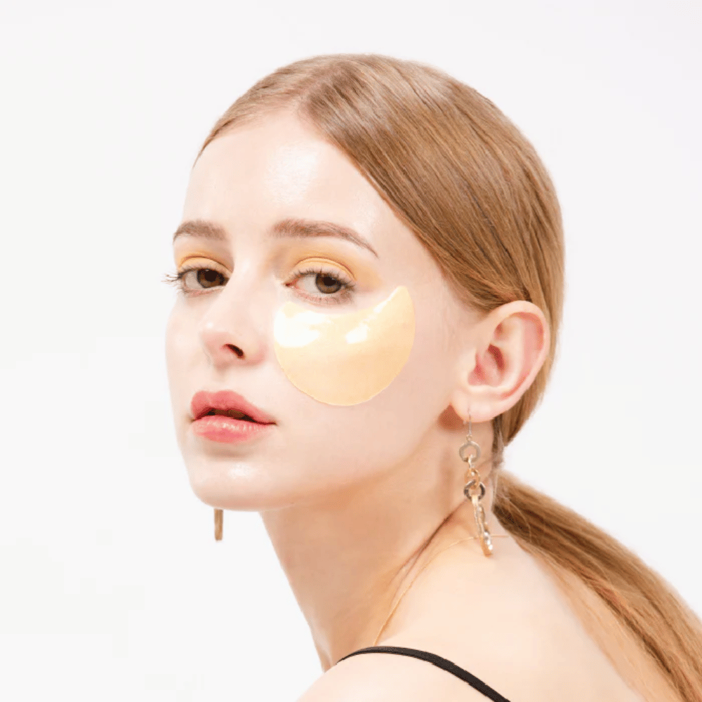 Modell har på seg en gullskimrende hydrogel eye patch under øyet for en glødende effekt.