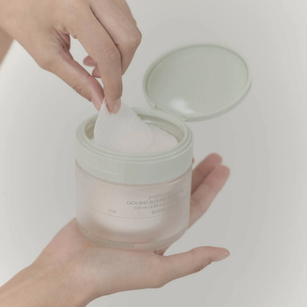 Hånd tar opp en toner pad fra krukken Celimax Ji Woo Gae Cica BHA Blemish Toner Pad, perfekt for uren hud.