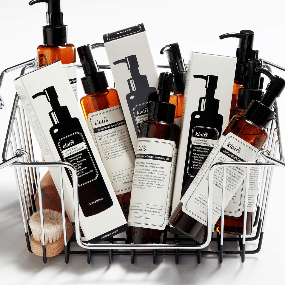 En minihandlevogn fylt med hudpleieprodukter fra Klairs, inkludert Gentle Black Deep Cleansing Oil i gjennomsiktige flasker med svarte pumper og matchende emballasje.