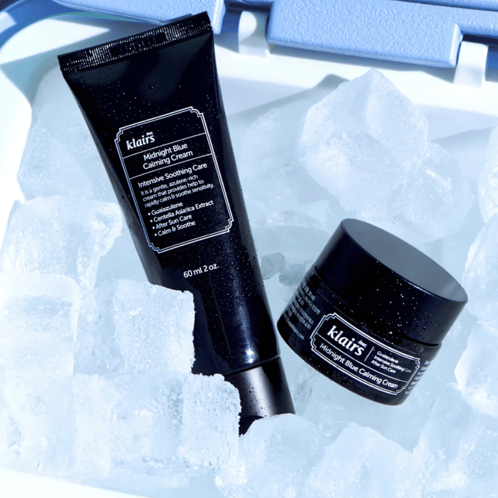 En tube og krukke av Klairs Midnight Blue Calming Cream ligger på isbiter, med fokus på beroligende og fuktighetsgivende egenskaper, mot en blå bakgrunn.