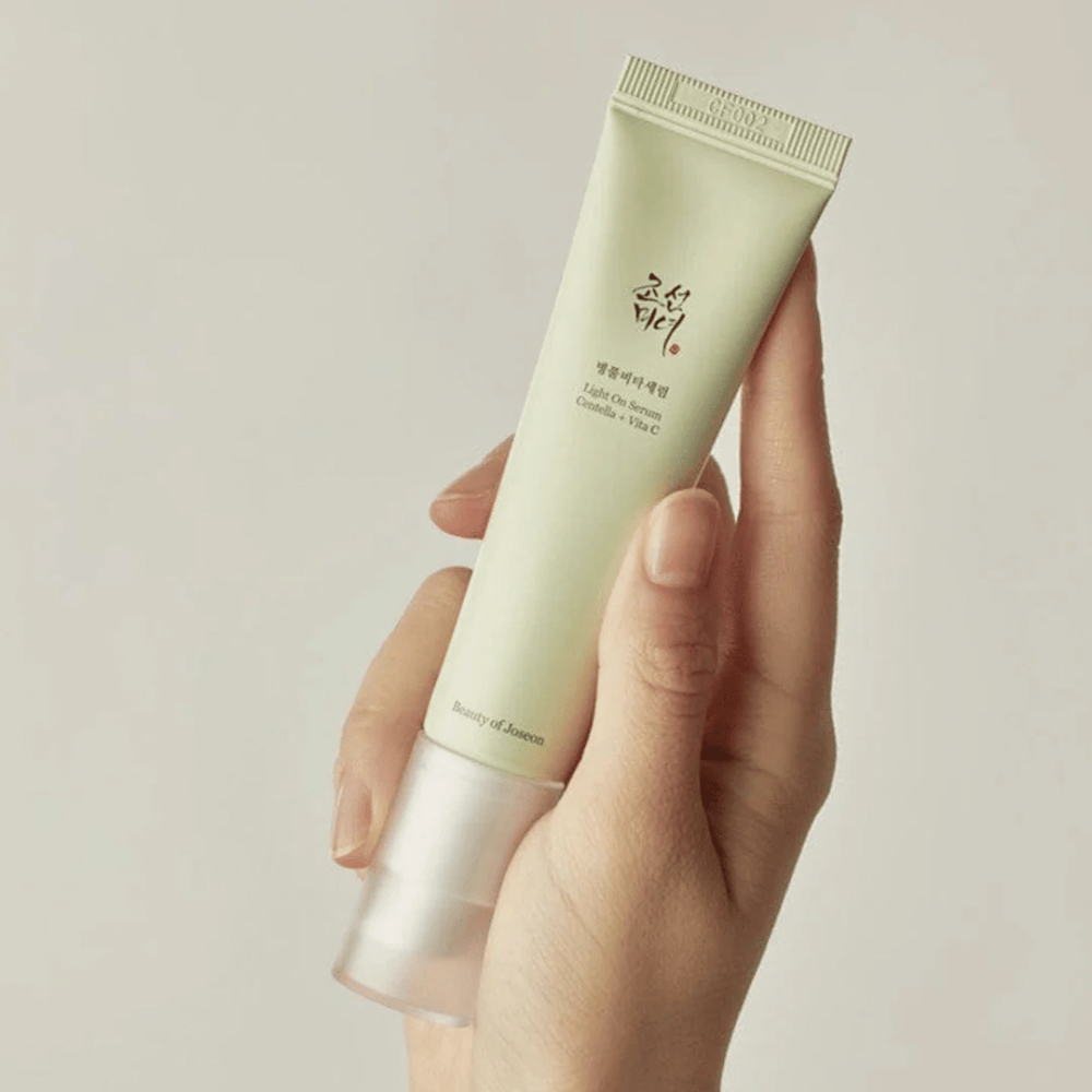 En hånd holder i Beauty of Joseon Light On Serum med Centella og vitamin C, i en lysegrønn tube med minimalistisk design mot en nøytral bakgrunn.