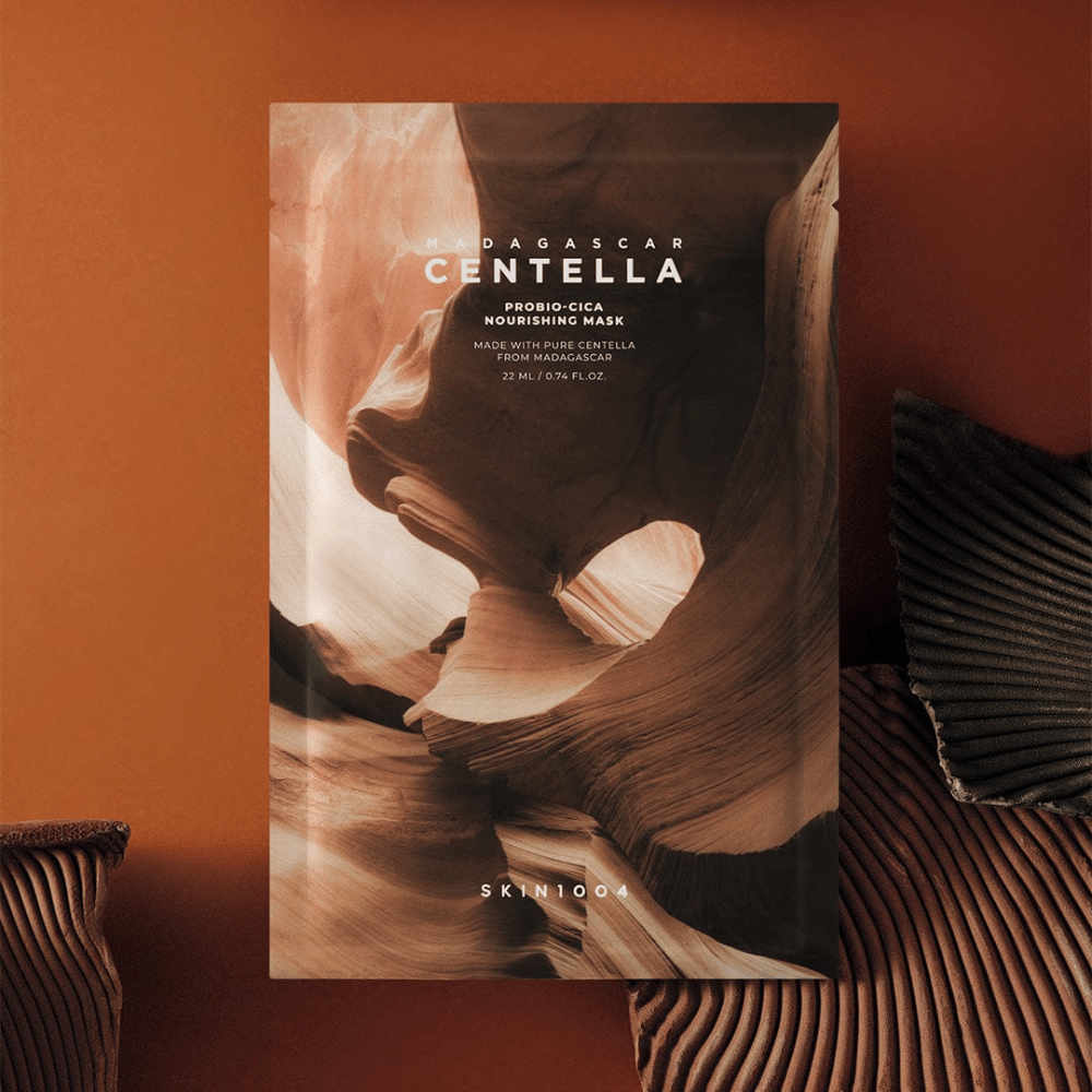 Sheet mask-emballasje fra SKIN1004 mot varm brun bakgrunn med naturinspirert design.