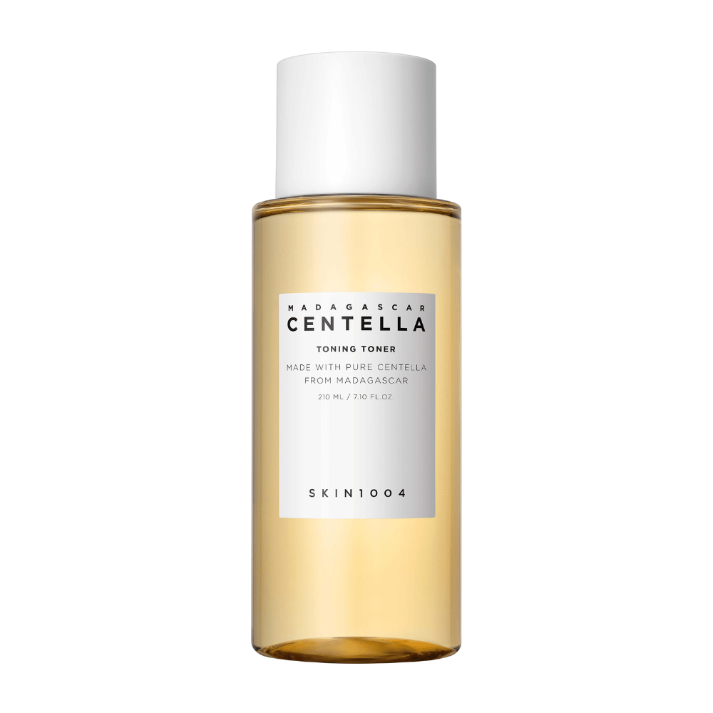 Bildet viser en flaske med hudpleietoner, merket "Madagascar Centella Toning Toner" fra SKIN1004. Produktet er oppgitt å inneholde 210 ml eller 7.10 fl.oz og er laget med ren Centella fra Madagaskar. Emballasjen er enkel og stilren med en gjennomsiktig flaske og gylden toner væske inni, noe som gir en følelse av luksus og renhet. Varemerkets logo SKIN1004 er tydelig synlig i den nedre delen av etiketten.