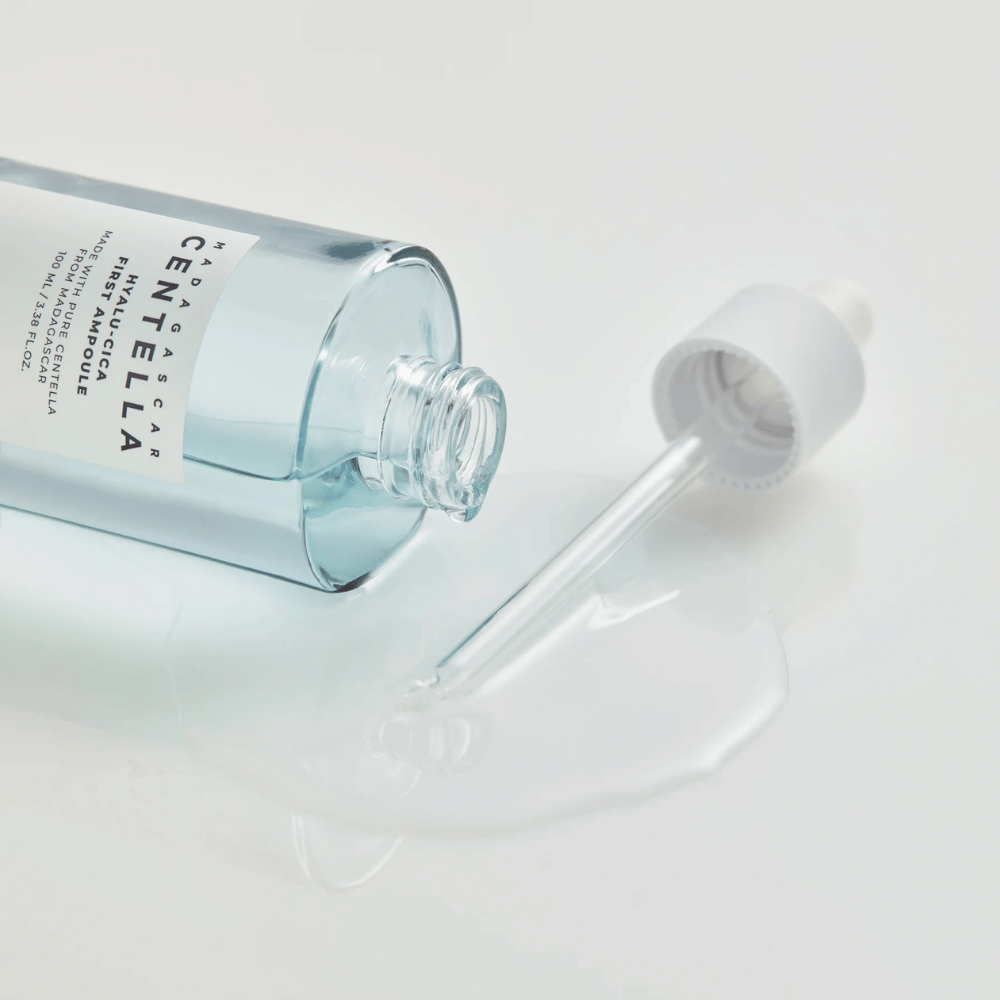 Nærbilde av åpen flaske Skin1004 Madagascar Centella Hyalu-Cica First Ampoule med pipette liggende og serum spredt på hvit overflate.