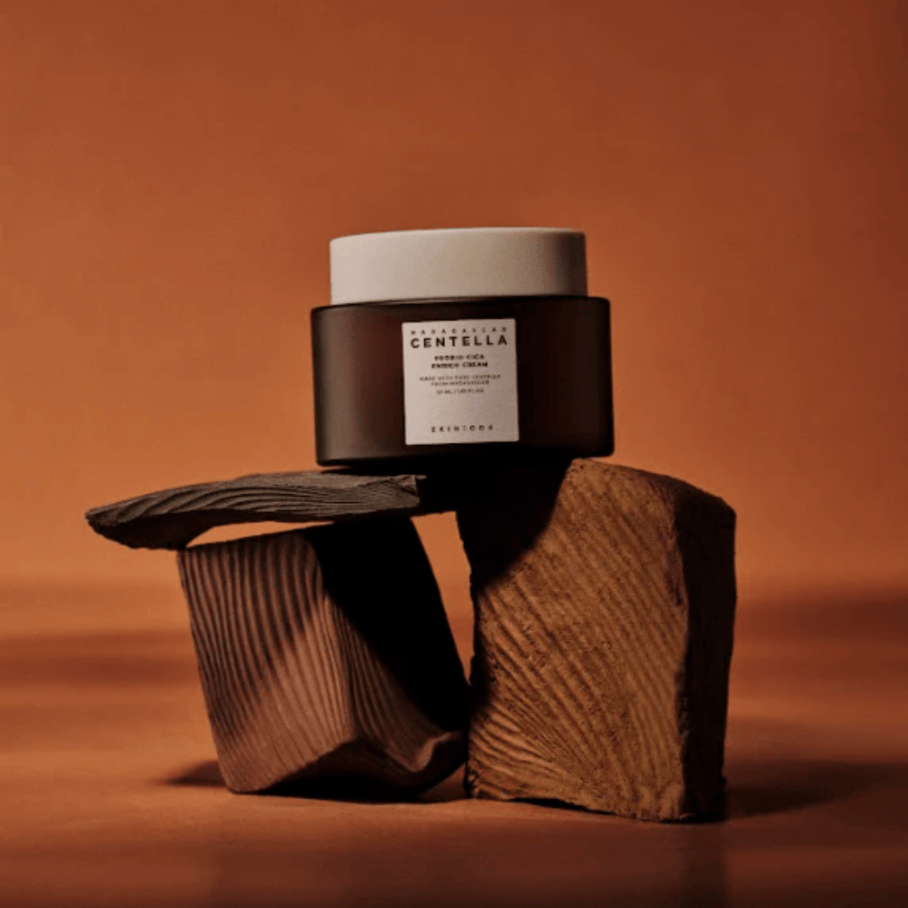 SKIN1004 Madagascar Centella Probio-Cica Enrich Cream i elegant brun glasskrukke på dekorative treblokker – næringsrik koreansk ansiktskrem som styrker hudbarrieren.