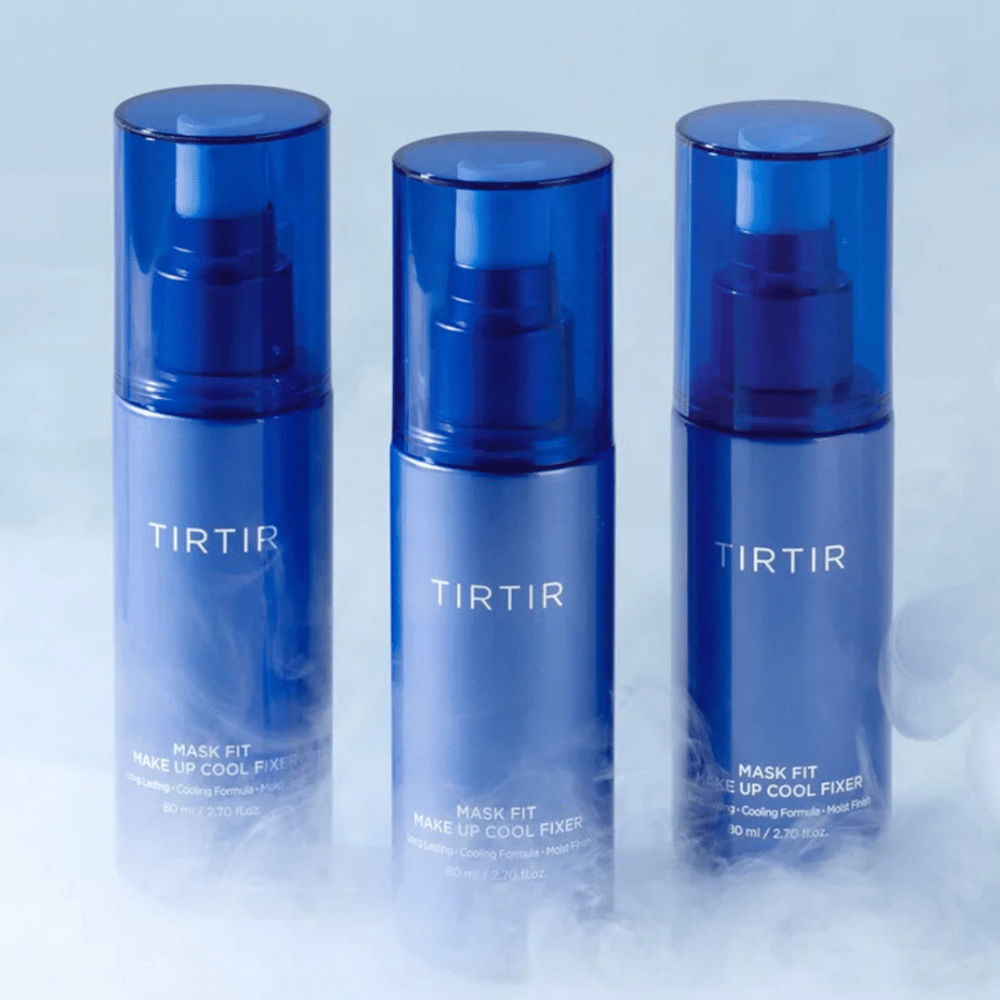 Tre blå sprayflasker med "TIRTIR Mask Fit Make Up Cool Fixer" på etiketten. Hver flaske rommer 80 ml (2,70 fl. oz.) og er utformet for å gi en avkjølende følelse og langvarig sminke. Flaskene står på en lys bakgrunn med tåke for å skape en atmosfære av friskhet.