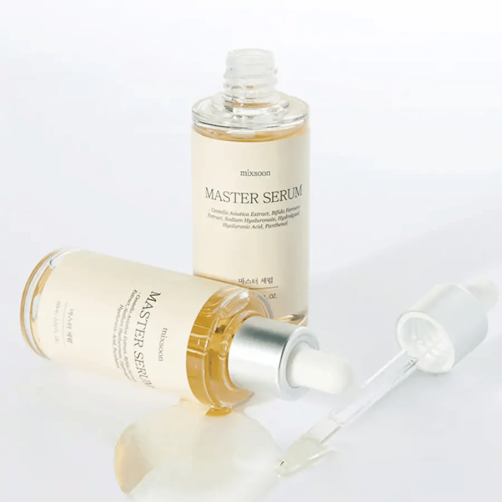 To flasker Mixsoon Master Serum, en stående og en liggende med åpen pipette, hvor serumet har sølt ut på en hvit overflate.