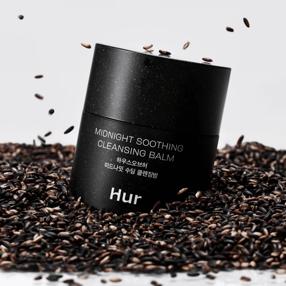 Hvordan Midnight Soothing Cleansing Balm i svart krukke plassert på svarte frø. Beroligende rensebalm som løser opp sminke og urenheter samtidig som huden pleies.