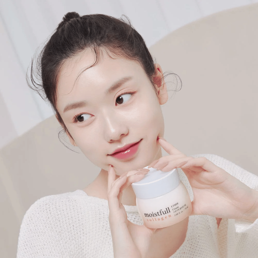 Kvinne holder en boks "Moistfull Collagen Cream", hvit trøye, smilende.
