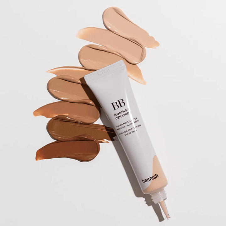 Heimish Moringa Ceramide BB Cream omgitt av flere nyanseprøver i ulike hudtoner. Bildet viser produktets brede fargeutvalg og den kremete konsistensen som gir naturlig dekning og jevn hudtone.