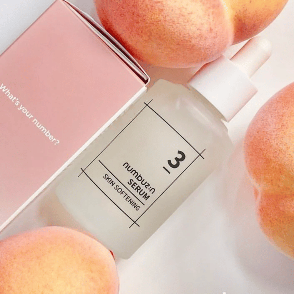 Flaske med numbus:in No.3 Skin Softening Serum omgitt av ferskener og en rosa eske med teksten "What's your number?".