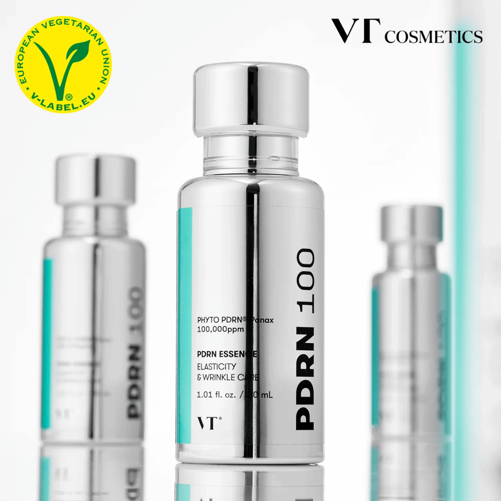 Flere sølvfargede flasker av VT PDRN 100 Essence står på rad, med tydelig merking om 100,000 ppm PDRN og fokus på elastisitet og rynkepleie. Øverst vises logoen for VT Cosmetics og et V-merke for vegetarisk innhold.