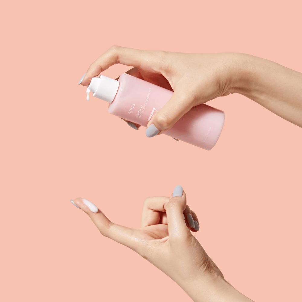 Bildet viser noen hender som holder en flaske med ANUA Peach 77% Niacin Conditioning Milk. Dette hudpleieproduktet ser ut til å ha en melkeaktig konsistens og er designet for å pleie og forbedre hudens tilstand.