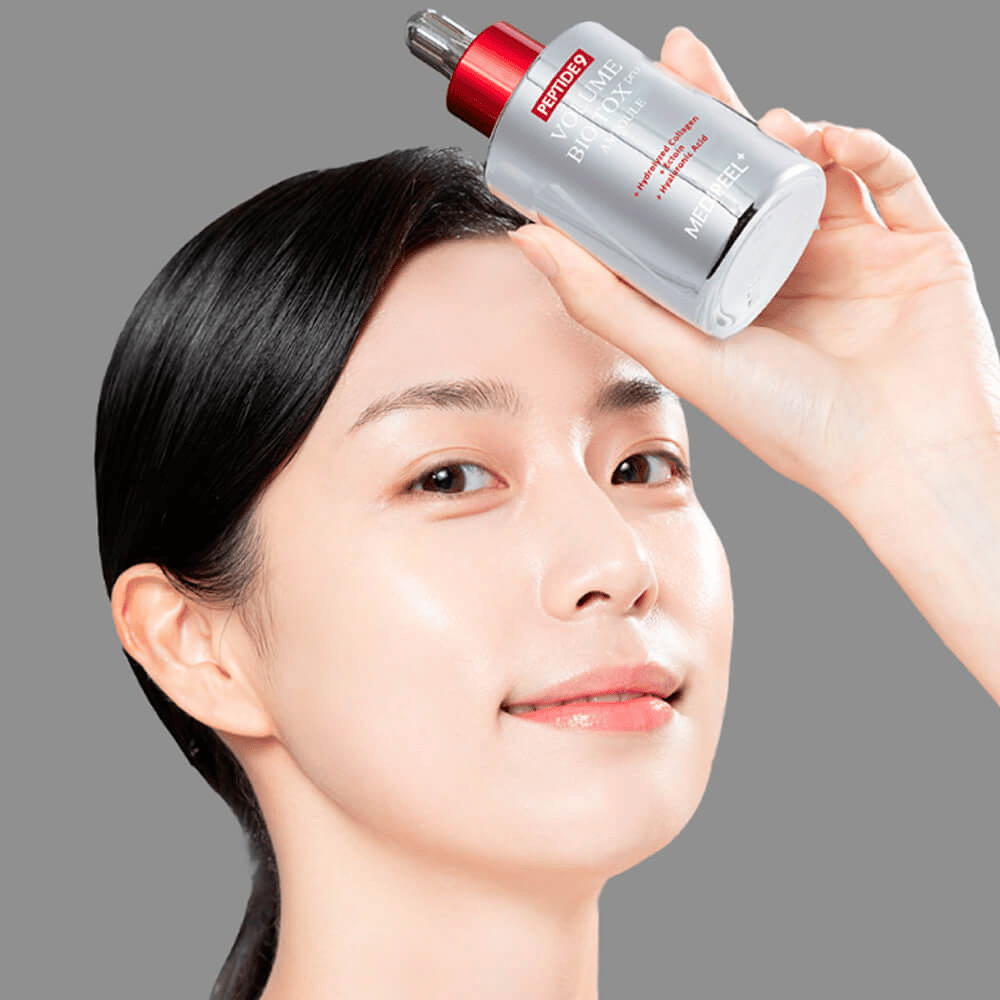 Person holder opp MEDI-PEEL Peptide 9 Volume Bio Tox Pro Ampoule mot pannen. Huden ser fuktet og strålende ut – serumet styrker elastisitet og fasthet.