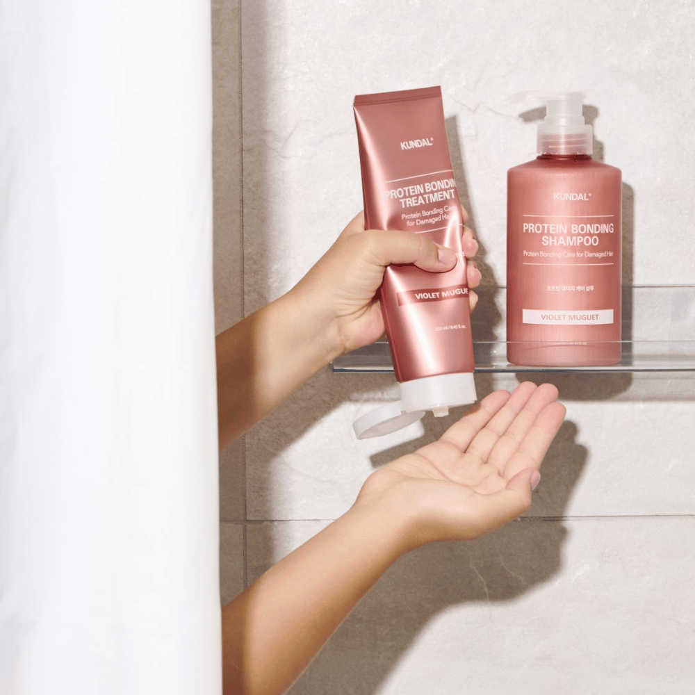KUNDAL Protein Bonding Treatment Violet Muguet brukes i dusjen, med Protein Bonding Shampoo plassert på hyllen ved siden av.