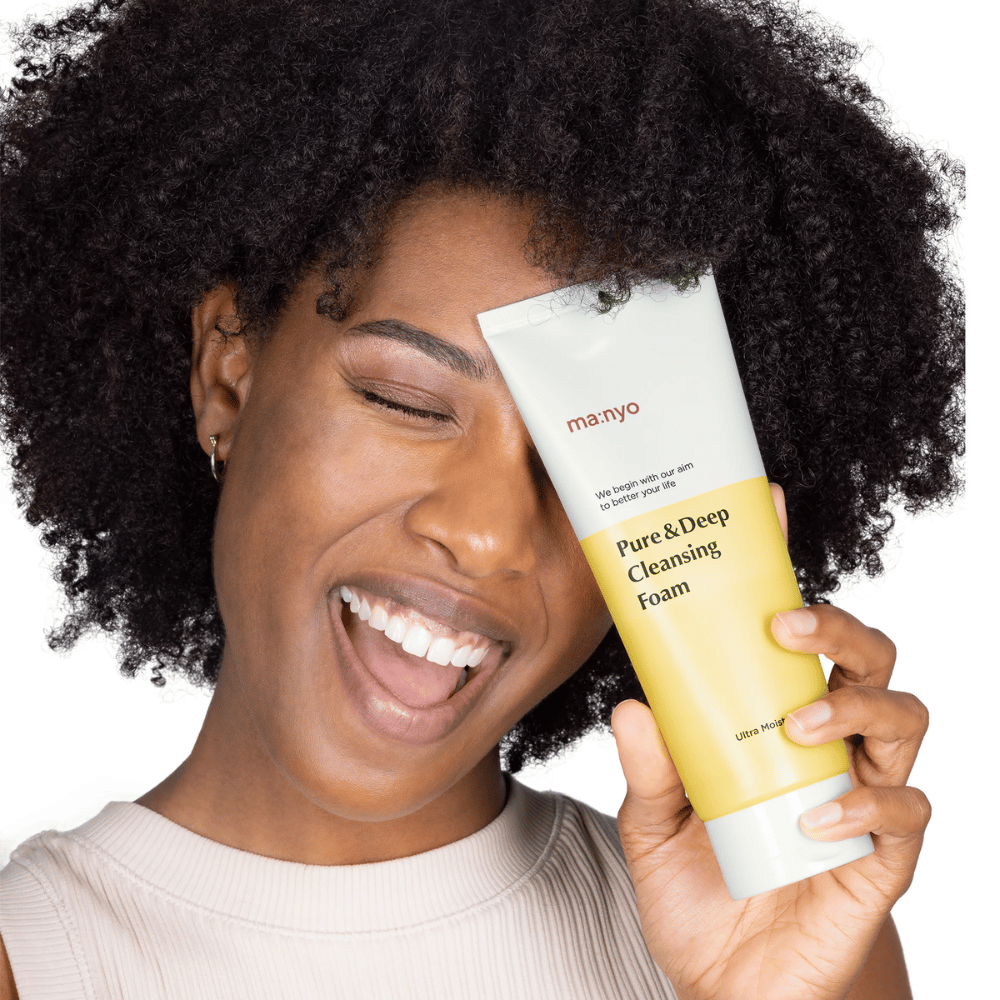 Kvinne med krøllete hår holder Ma:nyo Pure & Deep Cleansing Foam – en skånsom koreansk rens som effektivt fjerner smuss og sminke uten å tørke ut huden.
