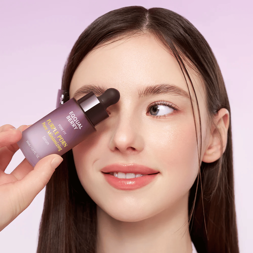 Ung kvinne med glatt hud holder en flaske Equal Berry Purple PDRN Pore Minimizing Serum mot pannen, mot en lys lilla bakgrunn.
