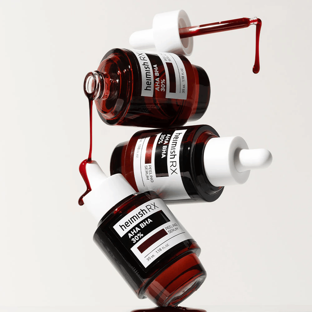 Tre flasker Heimish RX AHA BHA 30% Peeling Serum i en dynamisk komposisjon, med rødfarget serum som drypper fra pipettene.