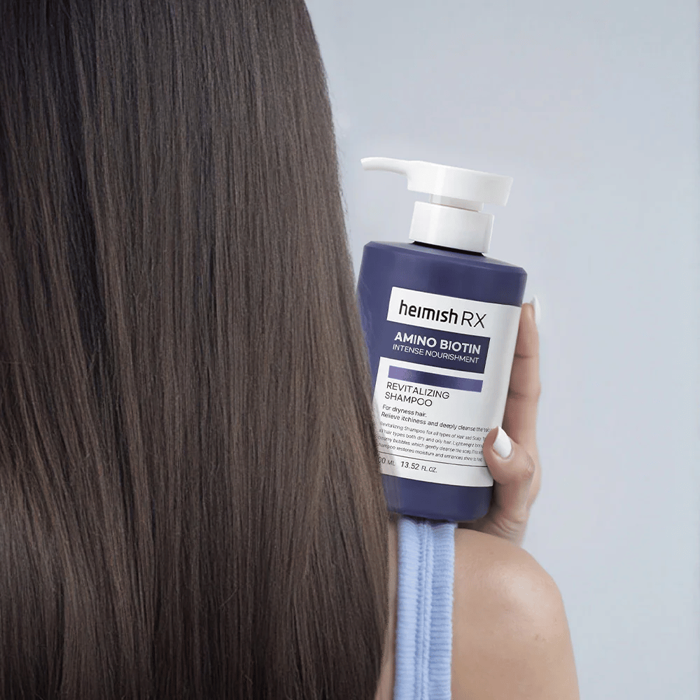 Heimish RX Amino Biotin Revitalizing Shampoo holdes i hånden mot langt, glansfullt hår – viser resultatet av intensiv næring og fuktighet for tørt hår.