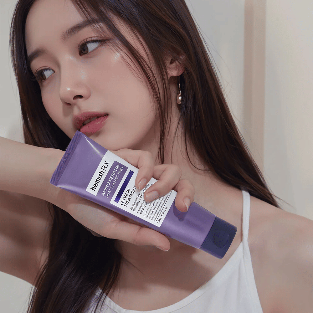 Kvinne med langt, glansfullt hår holder i Heimish RX Amino Keratin Leave-In Treatment – viser produktet som et pleiende og varmebeskyttende steg i hårpleierutinen.
