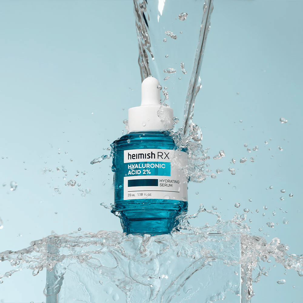 Heimish RX Hyaluronic Acid 2% Hydrating Serum plassert på en isaktig overflate med vann som spruter rundt, som symboliserer intens fuktighet og friskhet.