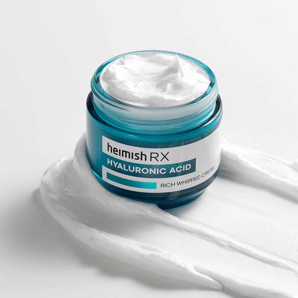 Heimish RX Hyaluronic Acid Rich Whipped Cream i en blå glasskrukke med rik og luftig konsistens, spredt på en hvit bakgrunn. Intensivt fuktighetsgivende ansiktskrem med hyaluronsyre for dyp fuktighet og myk hud.